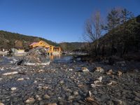 a small river flowing in to a wooden house on the top of a hill with buildings nearby