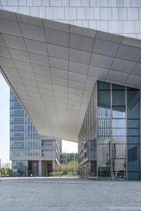 a white and gray modern building with glass windows on both sides of it with a sidewalk below the building that is a rectangular walkway