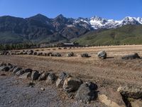 large rocks in a dirt field in front of a mountain range with snow capped peaks in the distance