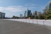 a parking lot with tall buildings in the background with red fences on it and a sky scraper to the side