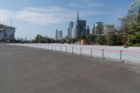 a parking lot with tall buildings in the background with red fences on it and a sky scraper to the side