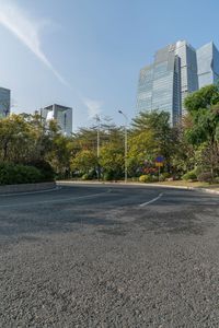 a deserted empty street with many tall buildings and plants around it and trees growing on either side