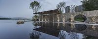 the reflection of the building is in a pool of water near a stone wall and trees