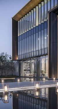 outdoor swimming pool near a tall building with glass windows and lights on the outside of it