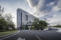 a long building with a parking lot in front of it and trees and bushes and a street