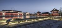 a chinese courtyard and lake with buildings around it at night lit up in brightly colors