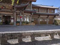 a bench is near a stone wall and building area in china that has a large wooden and asian style front