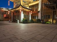 a building at night with a stone floor and chinese lanterns above it at the entrance