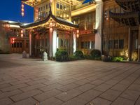 a building at night with a stone floor and chinese lanterns above it at the entrance