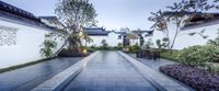 a walkway leading to a building surrounded by garden plants and trees and lights on at dusk