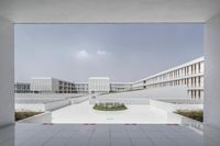 several buildings surrounded by white walls and grey flooring, in a courtyard with trees growing inside