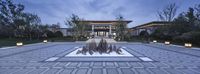 a large building has a fountain in the middle of the yard with lights on it