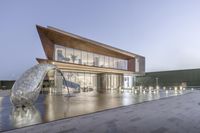 an outdoor statue stands by a building with a glass wall and sliding door on top