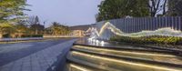 some stairs, fountains, and trees by the ocean side line are illuminated at dusk