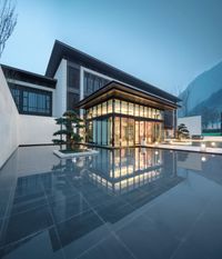 a modern building lit up at night in the mountains behind it with stairs and a pool