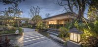 a walkway leading to a modern home with a fountain area, garden, and outdoor lighting