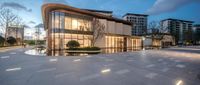 an apartment in the twilight with lights shining on it and water features and is illuminated in the foreground