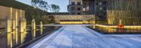 a beautiful courtyard area with a fountain and lots of greenery in the background, lit by a single street lamp