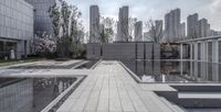 a large concrete walkway and some water features with tall buildings in the distance behind it