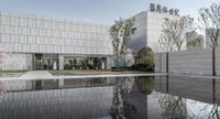 the museum and gardens are reflectiond in water on a sunny day with trees lining the courtyard