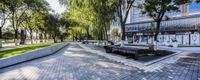 a park area with stone benches and trees along the walkway, near buildings and street