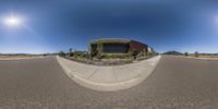 a fisheye shot of a circular building in a desert area with the sun in the background