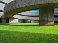 the circular building has green grass and tall concrete columns in it with the blue sky in the background