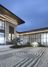 a circular rock pathway runs through a garden at the edge of a building with several windows