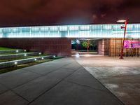 a view of a building and walkway lit up at night with light on it's surface