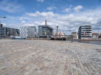 this view shows a paved street near water with buildings in the background and a fenced off area