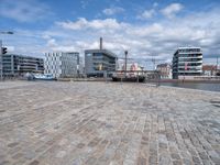 this view shows a paved street near water with buildings in the background and a fenced off area