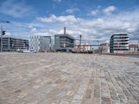 this view shows a paved street near water with buildings in the background and a fenced off area