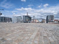 this view shows a paved street near water with buildings in the background and a fenced off area