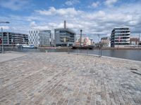 this view shows a paved street near water with buildings in the background and a fenced off area