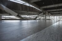 a floor with concrete tiles underneath a metal structure with beams above it and sunlight coming through the windows