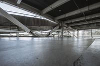 a floor with concrete tiles underneath a metal structure with beams above it and sunlight coming through the windows