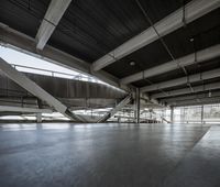 a floor with concrete tiles underneath a metal structure with beams above it and sunlight coming through the windows