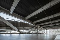 a floor with concrete tiles underneath a metal structure with beams above it and sunlight coming through the windows