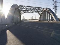 a metal bridge spanning over an empty road with power lines in the background under the sun