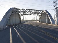 a metal bridge spanning over an empty road with power lines in the background under the sun