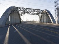 a metal bridge spanning over an empty road with power lines in the background under the sun