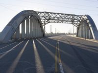 a metal bridge spanning over an empty road with power lines in the background under the sun