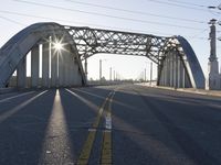 a metal bridge spanning over an empty road with power lines in the background under the sun