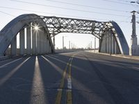 a metal bridge spanning over an empty road with power lines in the background under the sun