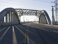 a metal bridge spanning over an empty road with power lines in the background under the sun