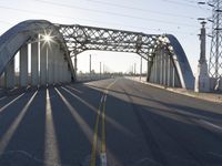 a metal bridge spanning over an empty road with power lines in the background under the sun