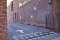 an intersection with directional signs in front of a brick wall and a closed gate in the background