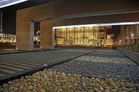a walkway with a few gravel, rocks, and a lit up building on the other side