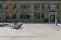 a bench sitting in front of a large brick building with many windows and an area with a sidewalk