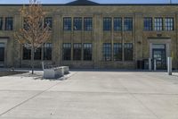 a bench sitting in front of a large brick building with many windows and an area with a sidewalk